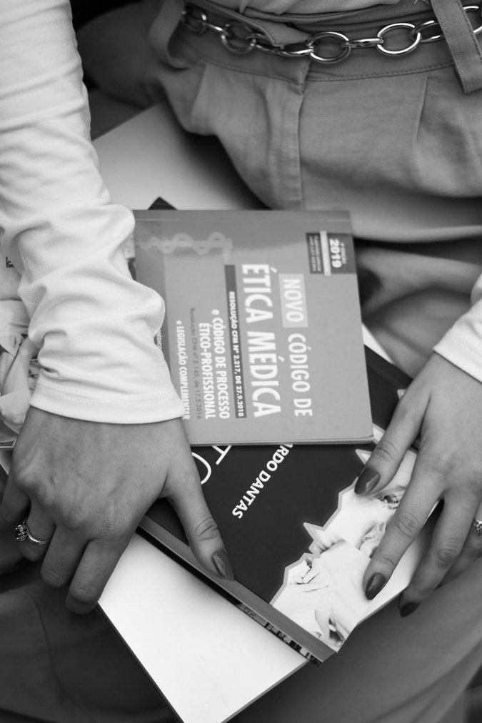Mãos segurando um exemplar do Código de Ética Médica, em preto e branco