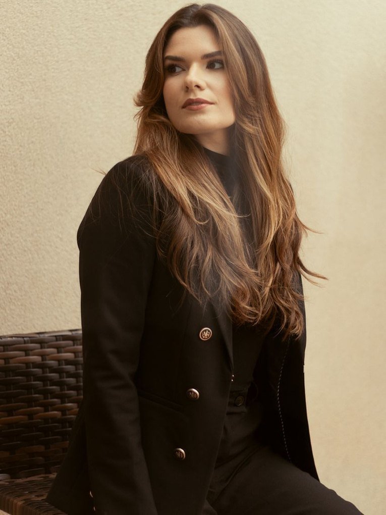 Isabelle Carapinha, advogada, sentada, de blazer preto, olhando para o lado