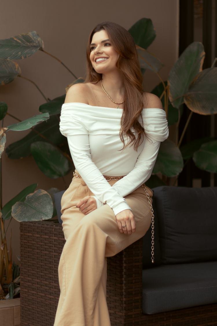 Isabelle Carapinha sorrindo, sentada, com plantas ao fundo